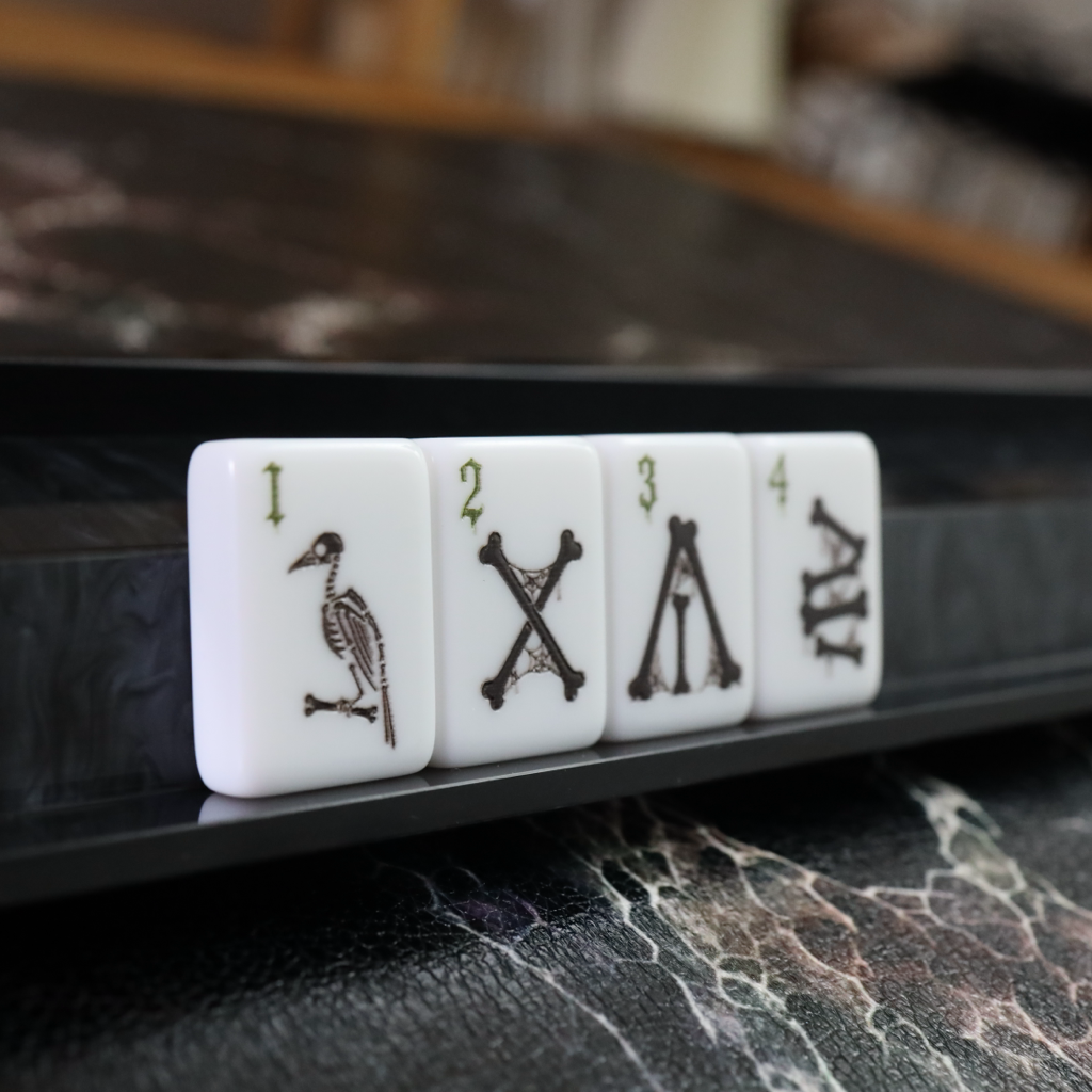 Four white mahjong tiles with black engraved symbols and numbers 1 through 4, resting on a glossy black mahjong board over a marble surface.