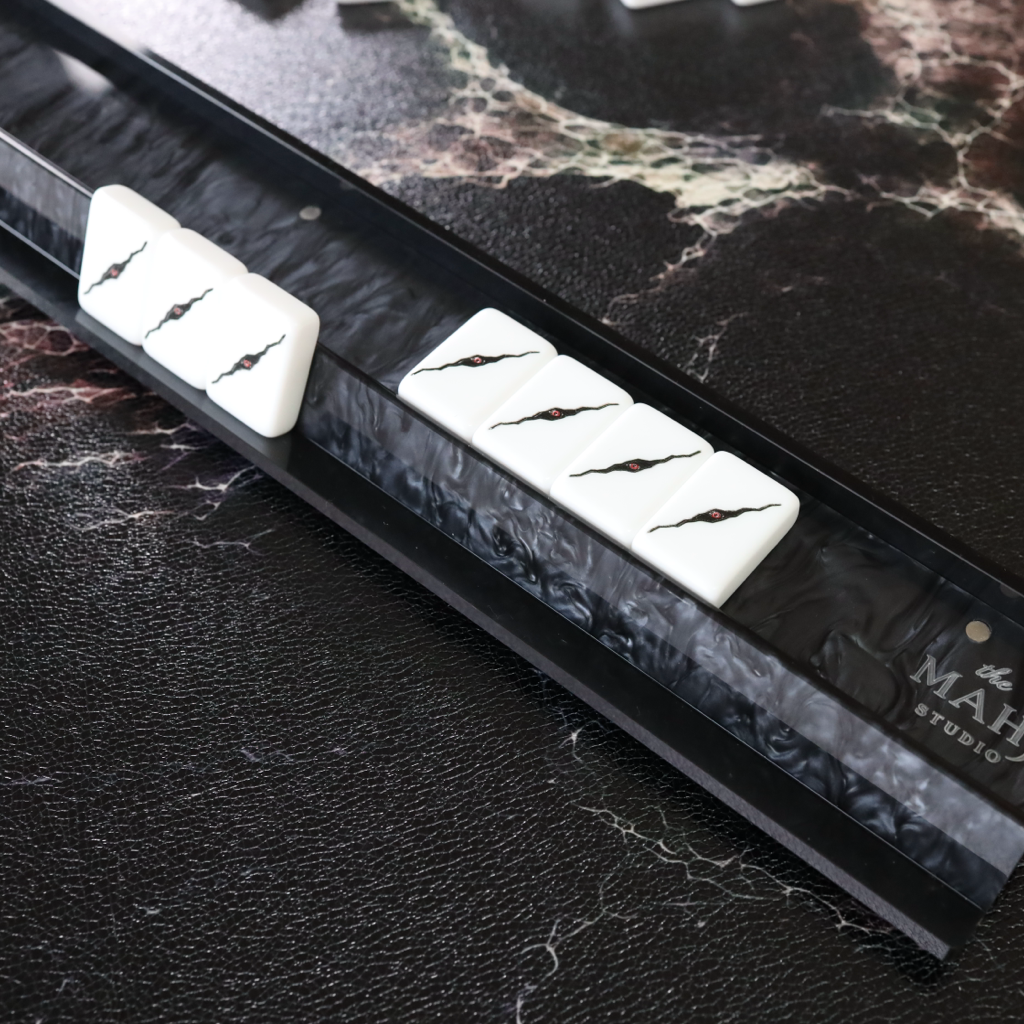 A close-up of a black mahogany-style guitar headstock with white pickguards featuring black lightning bolt graphics, resting on a dark marble surface.