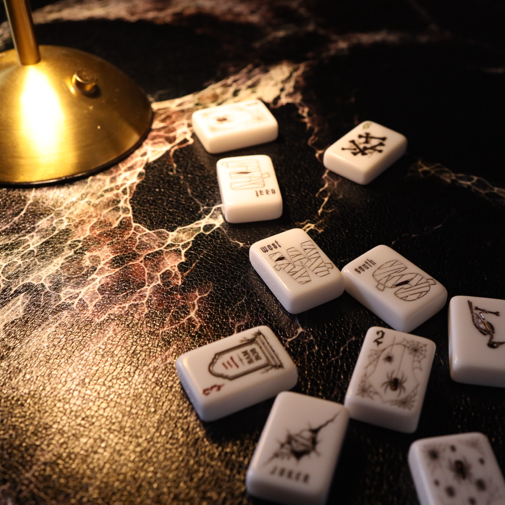 White Chinese mahjong tiles with black engraved symbols scattered on a dark, textured surface next to a brass lamp base.