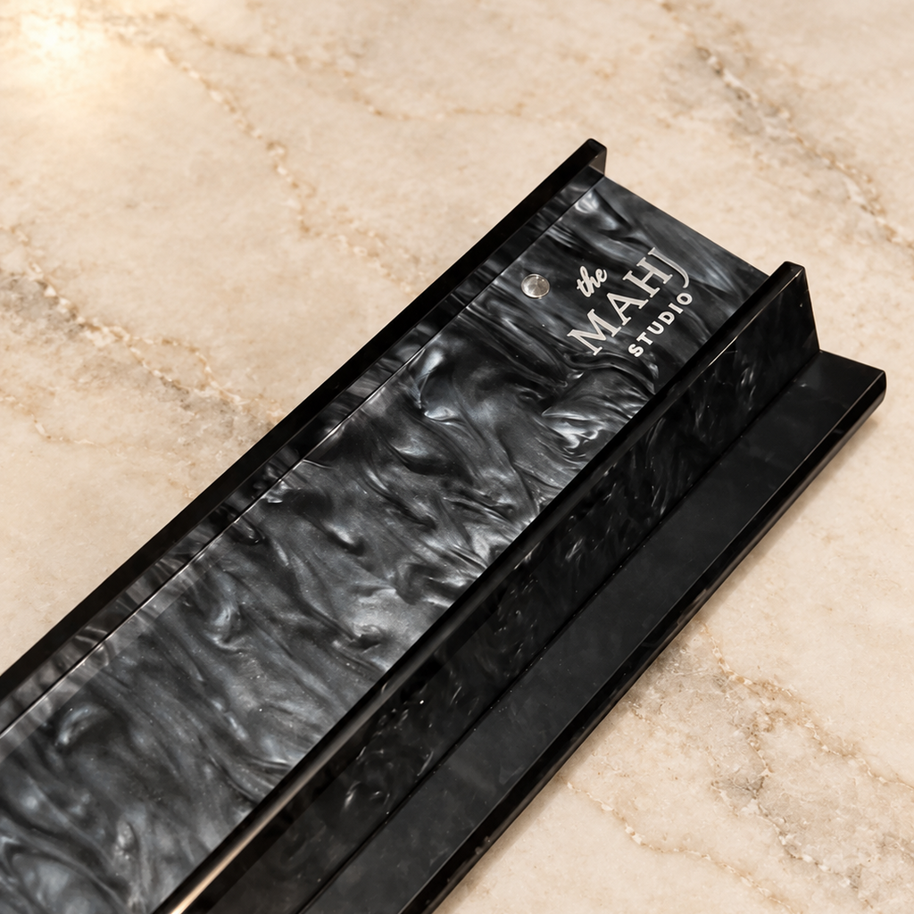 A close-up of a black marble fireplace insert with a wavy, textured pattern, resting on a beige marble floor. The brand name 'The MAH STUDIO' is clearly printed on the top surface.
