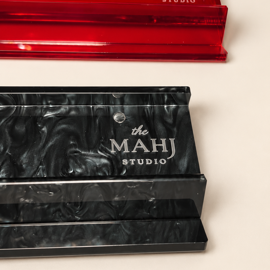 Two acrylic makeup sponges from The Mahj Studio, one translucent red and one black swirled marbled, displayed on a light beige background.