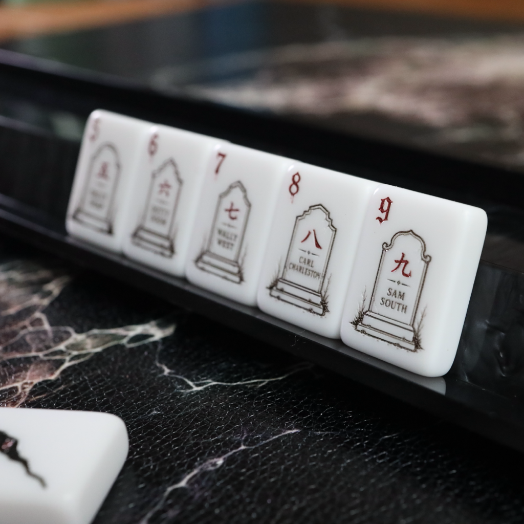 A close-up of white Mahjong tiles with black Chinese characters and red numbers, resting on a glossy black marble-like surface.