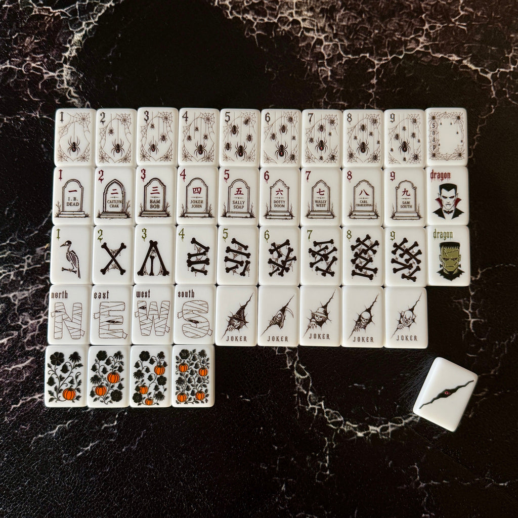 A set of white playing cards with black illustrations and symbols arranged in a grid on a dark marbled surface, with one card placed separately to the lower right.