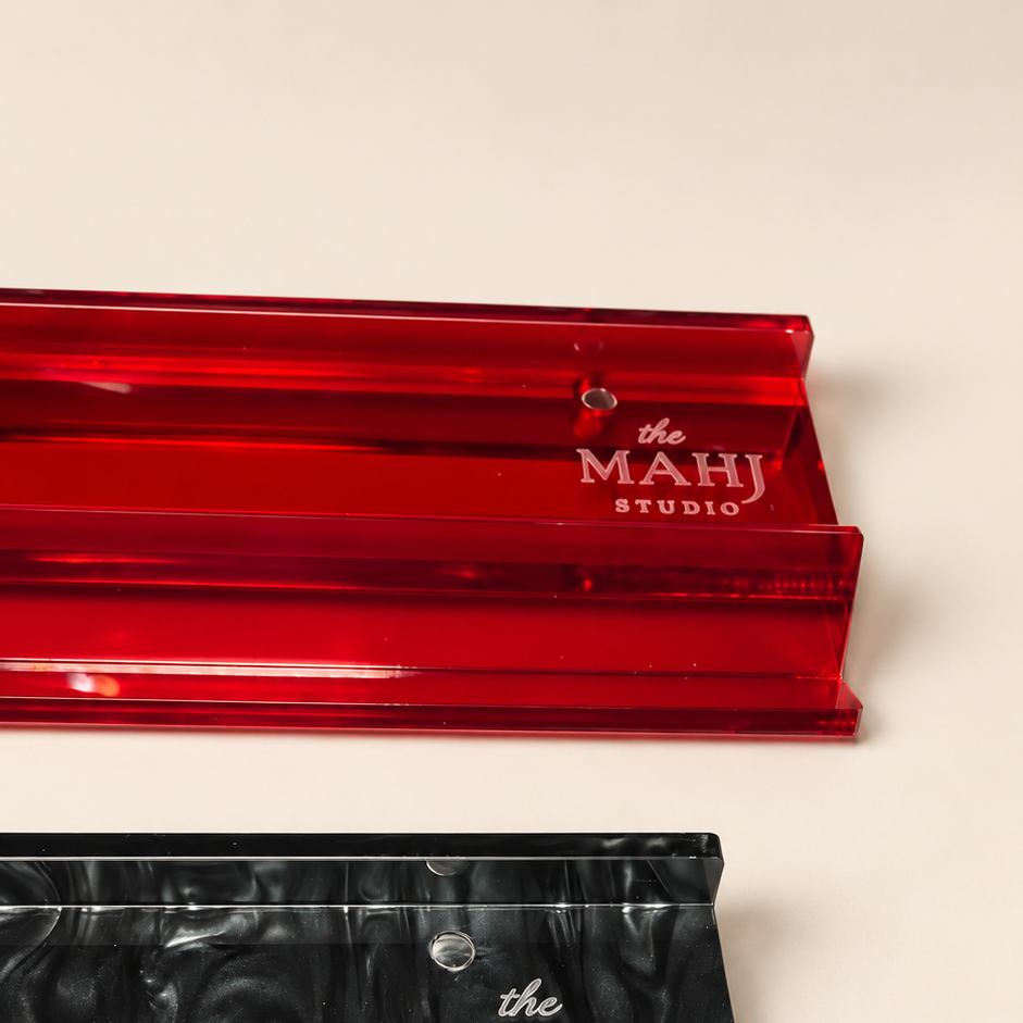 Two acrylic makeup sponges from The Mahj Studio, one translucent red and one black swirled marbled, displayed on a light beige background.