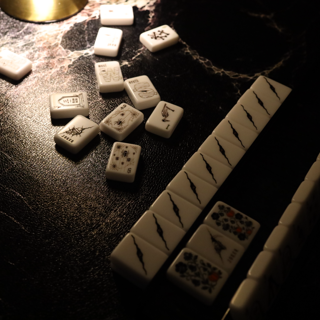 White mahjong tiles arranged in rows on a dark, textured surface under dramatic low lighting.
