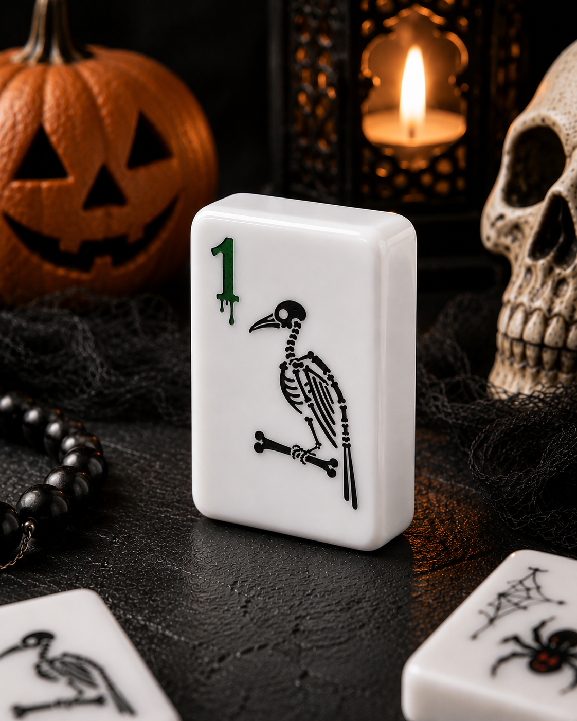 A Halloween-themed white mahjong tile featuring a black bird skeleton design and a green '1' in the corner, displayed on a dark surface with a jack-o'-lantern, skull, candle, and black beads in the background.