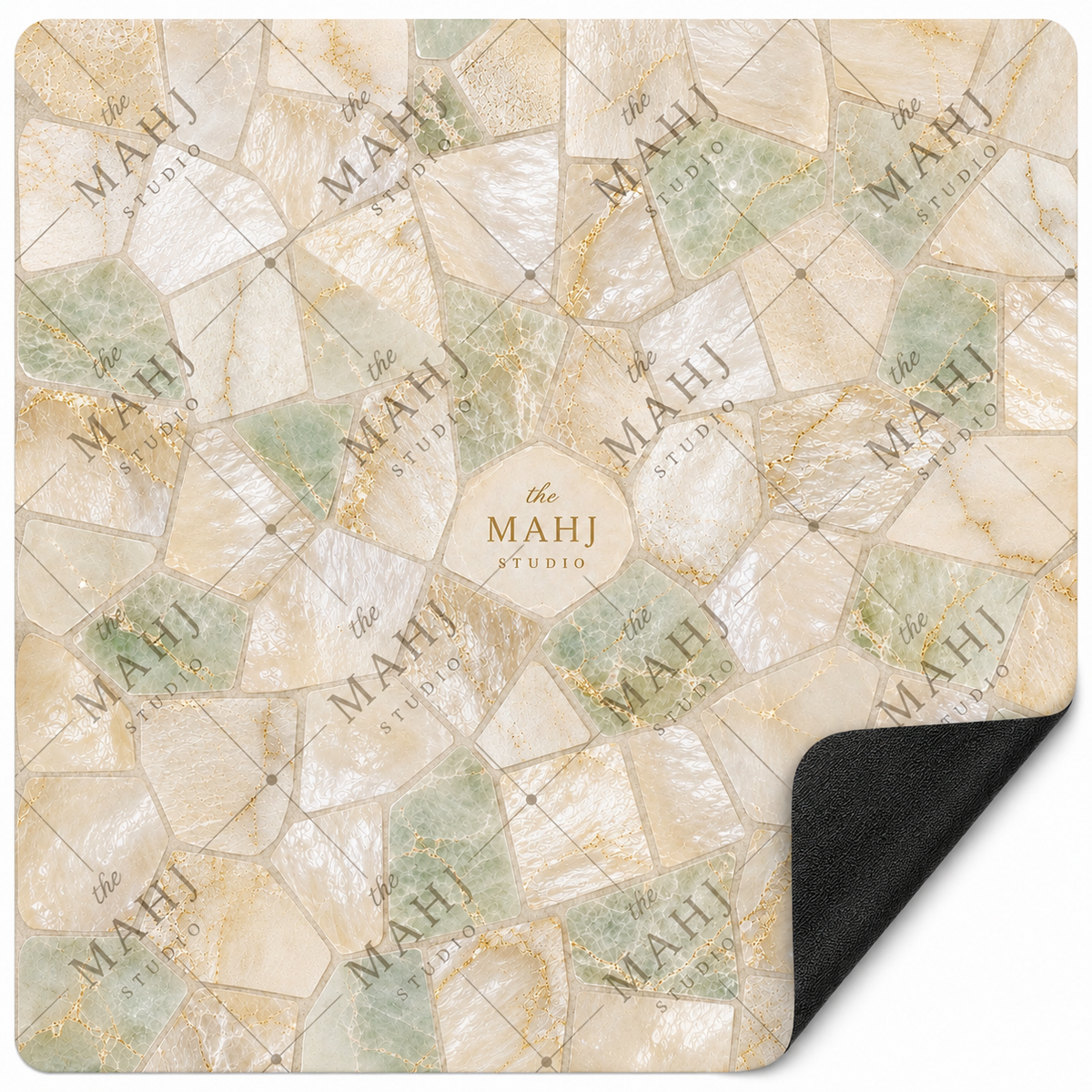 A square decorative mat or rug with a faux stone mosaic pattern in cream, beige, pale green, and gold veining, shown on a white background with one corner curled up to reveal a black backing. The brand name 'the MAHJ STUDIO' is watermarked across the design.