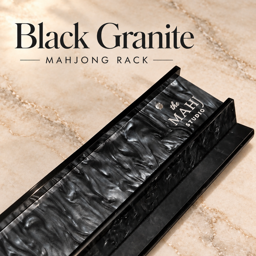 A black granite mahjong rack shown diagonally on a beige marble surface, with the text 'Black Granite MAHJONG RACK' at the top and 'the MAHJONG STUDIO' printed on the product.